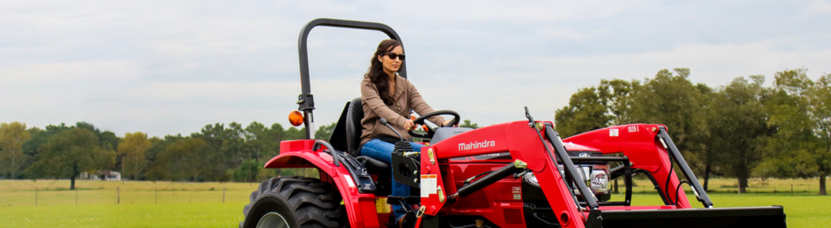 Woman operating a red Mahindra® tractor.